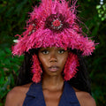 Person wearing a vibrant pink hat with feathers against a natural background