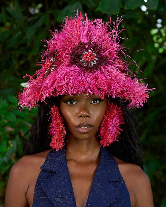 Person wearing a vibrant pink hat with feathers against a natural background