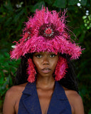 Person wearing a vibrant pink hat with feathers against a natural background